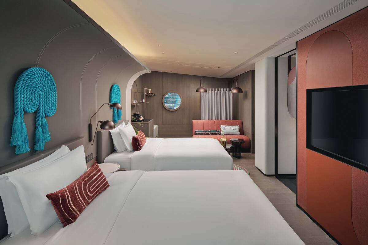 A modern hotel room with two beds, a TV, and a large mirror.