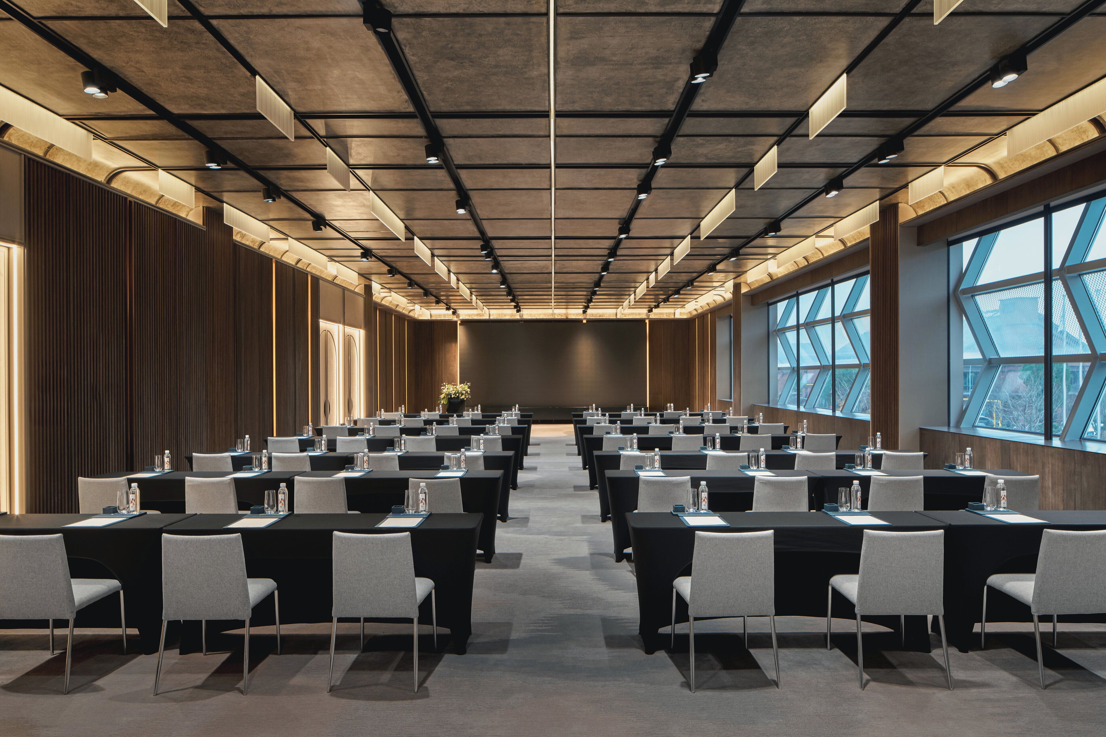 A conference room with rows of tables and chairs, large windows, and a modern ceiling design.
