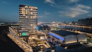 A modern hotel with a curved facade, a rooftop pool, and a view of a river and bridge. - Hotel Indigo Ningbo Riverside by IHG (Ningbo)