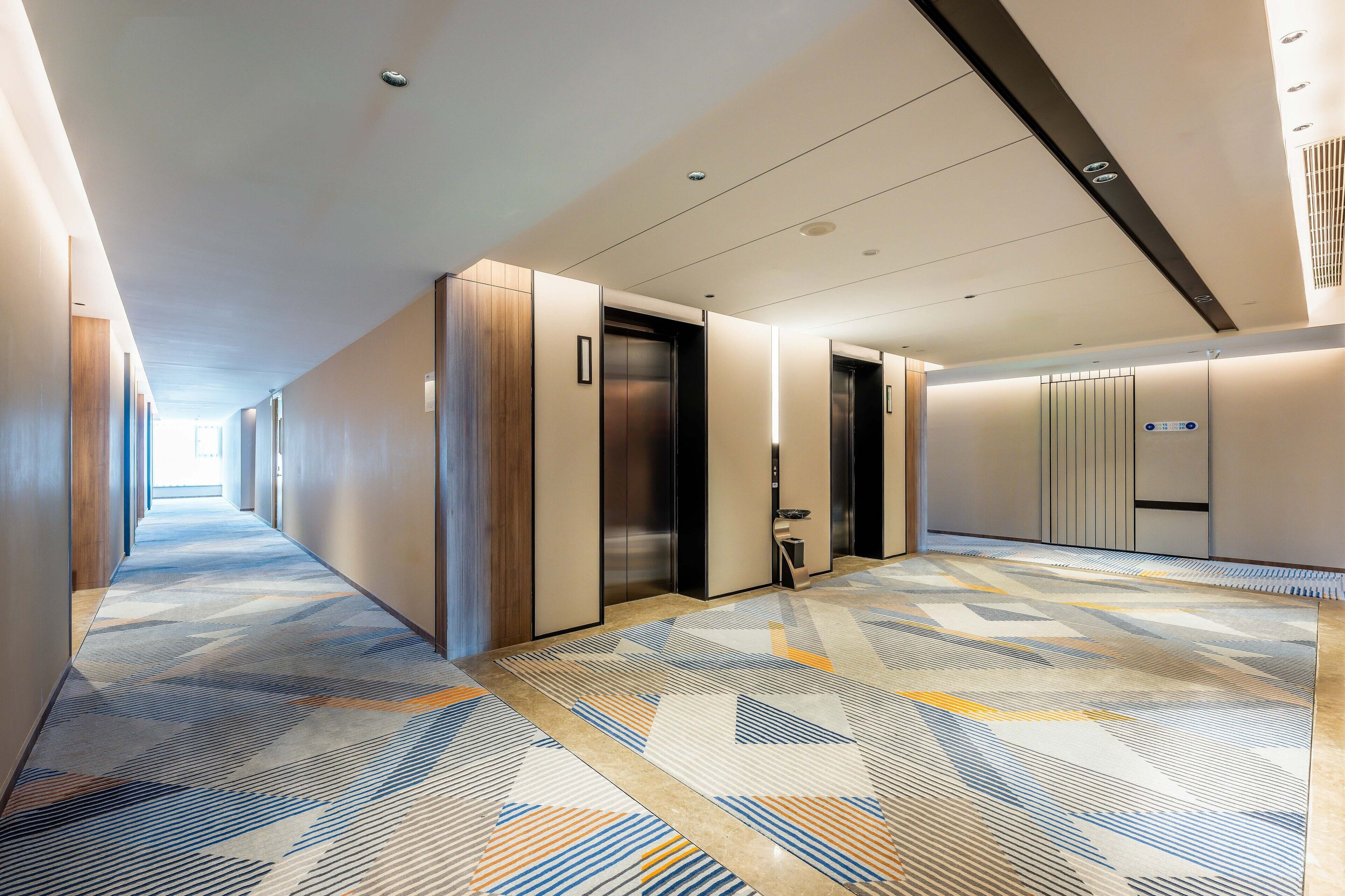 Un pasillo moderno de hotel con ascensores, una alfombra estampada y un diseño limpio y minimalista.
