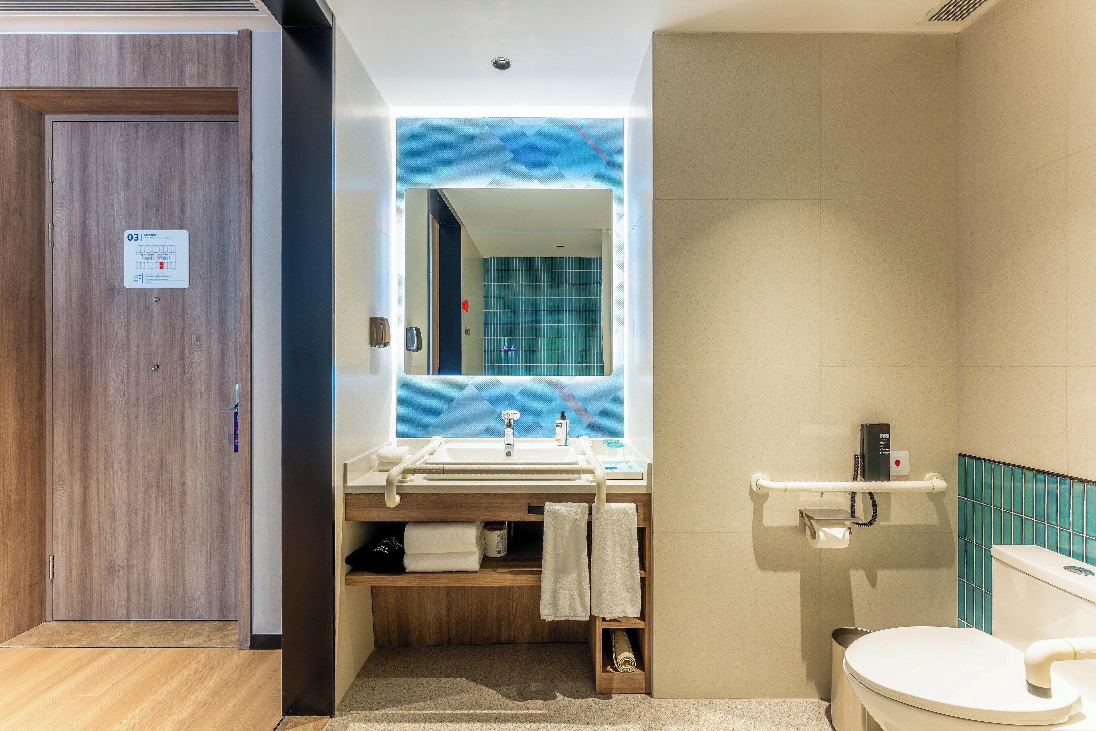 Un baño moderno con puerta de madera, un lavabo con toallero, un espejo y un inodoro.