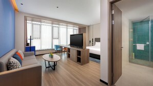 Una habitación de hotel moderna con televisión de pantalla plana, un sofá, una mesita pequeña y zona de ducha de vidrio.