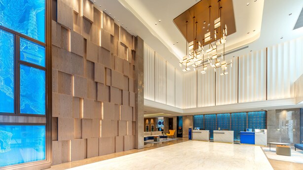 Un lobby espacioso con un mostrador de recepción moderno, un área de descanso y un ventanal con un diseño abstracto en azul.