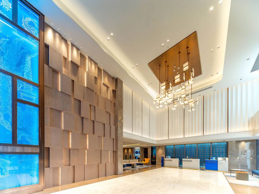 A spacious lobby with a modern reception desk, a seating area, and a large window with a blue abstract design.