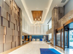 Un vestíbulo amplio con techo alto, luminarias modernas y un mostrador de recepción.