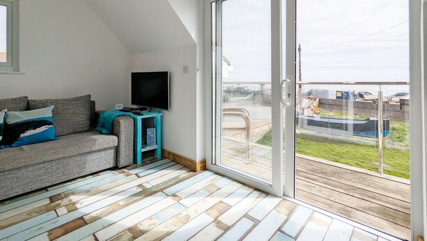 A room with a sofa, a television, and a sliding glass door leading to an outdoor area. - Sea Esta, Selsey - sleeps 4 guests  in 1 bedroom (Selsey)
