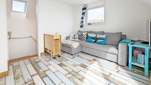 A cozy living room with a grey sofa, wooden side table, and a small bookshelf. - Sea Esta, Selsey - sleeps 4 guests  in 1 bedroom (Selsey)