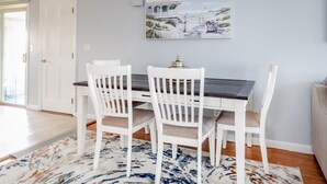 Un coin repas avec une table et quatre chaises blanches, un tableau au mur et un tapis à motifs sur le sol.