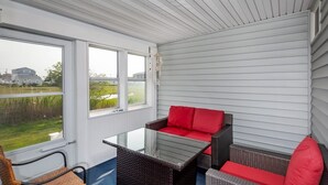 Un patio couvert avec une table en verre et des meubles en osier, donnant sur une pelouse.