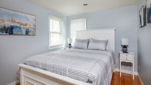 Une chambre à coucher avec un lit blanc, deux tables de chevet et un tableau accroché au mur.
