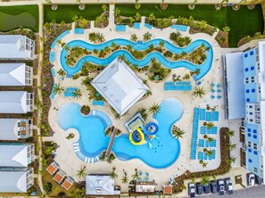 An aerial view of a resort with multiple swimming pools, sun loungers, and palm trees.