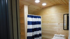 Une salle de bain aux murs lambrissés, avec un rideau de douche à rayures, une pile de serviettes blanches et un miroir au mur.