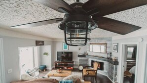 A modern living room with a ceiling fan, a fireplace, and a cozy seating area.