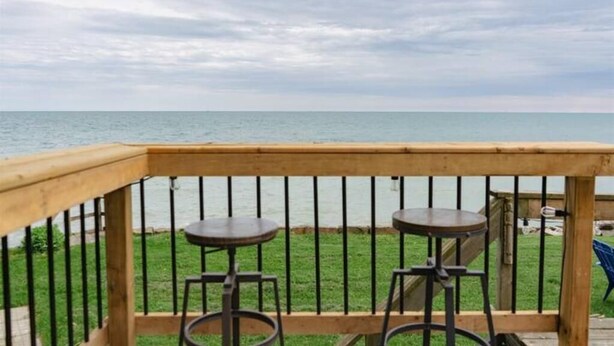 A wooden deck with two metal barstools facing a body of water.