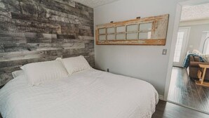A bedroom with a large bed, a rustic wooden wall, and a mirror with a distressed frame.