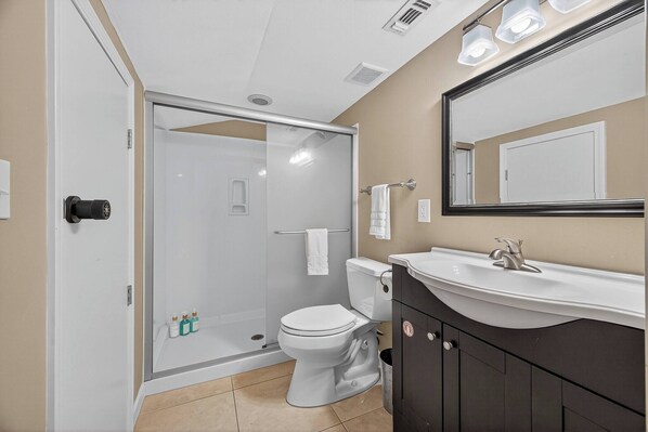 A modern bathroom with a glass shower enclosure, a white toilet, and a dark-toned vanity with a sink. - 10G, Sandy´s Beach Retreat (Destin)
