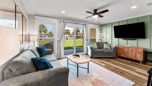 A modern living room with a grey sofa, a wooden coffee table, a grey armchair, and a television on the wall.