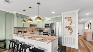 A kitchen with a central island, bar stools, pendant lights, and a refrigerator.