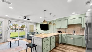 A modern kitchen with light green cabinets, a marble countertop, and a large island.