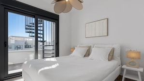 A modern bedroom with a large bed, a view of the outside, a ceiling light, and a wall-mounted artwork.