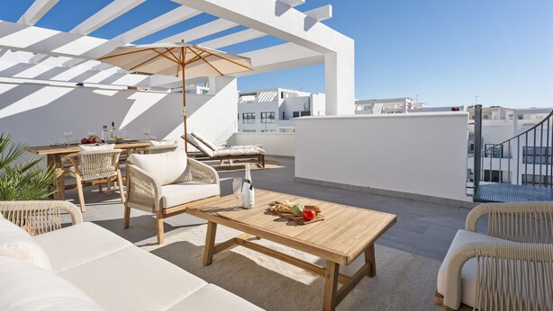 A rooftop terrace with outdoor furniture, a wooden table, and a pergola providing shade.