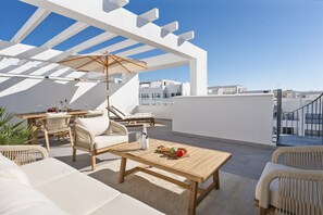 Eine Dachterrasse mit Gartenmöbeln, einem Holztisch und einer Pergola, die Schatten spendet.