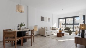A modern living room with a dining area, featuring a round table, wicker chairs, a sofa, and a coffee table.