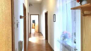 A hallway with wooden flooring, a wooden door on the left, and a window with a view of flowers on the right. - Meeraner Parkresidenz (Meerane)