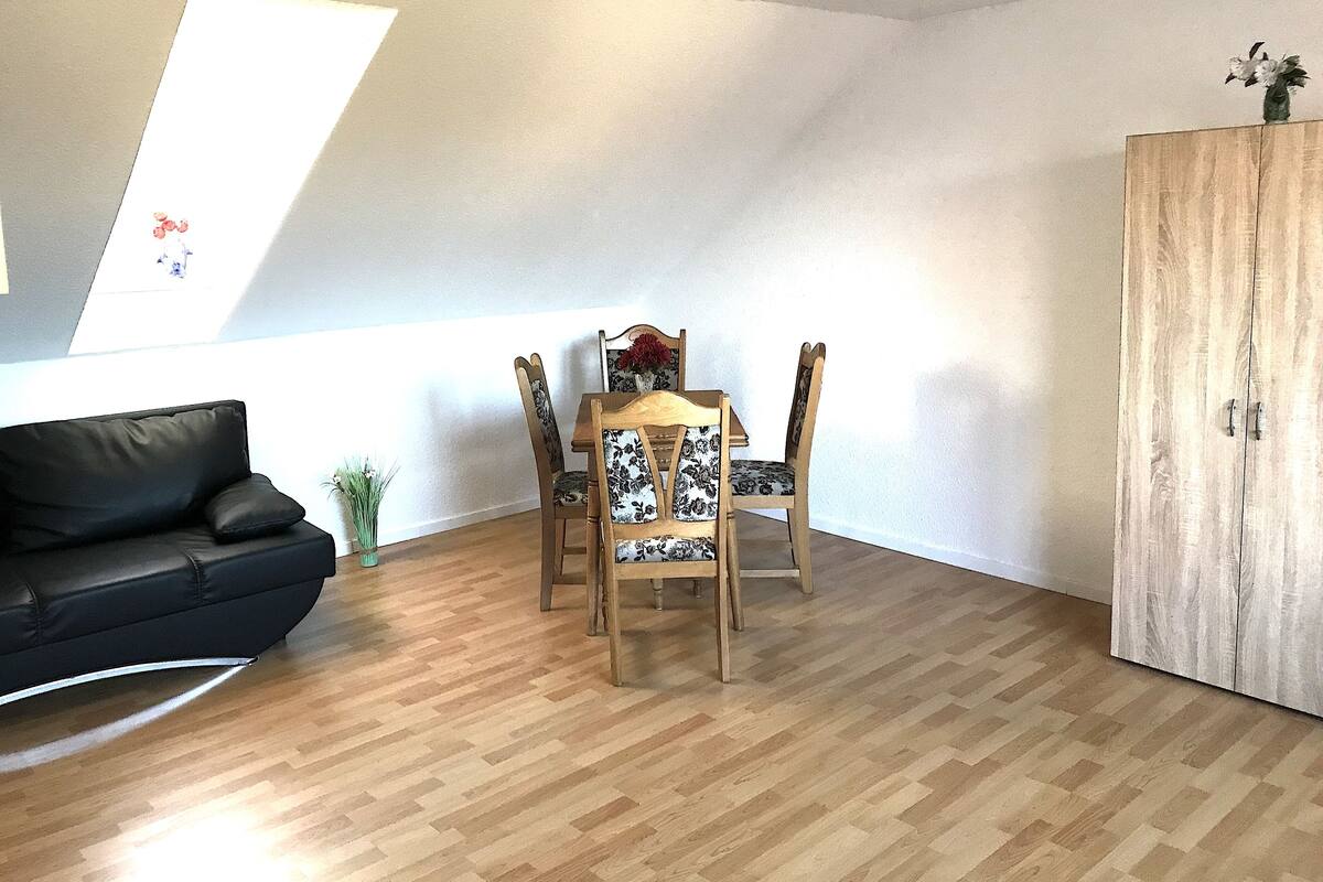 A room with a wooden dining table, four chairs, a black sofa, a wooden cabinet, and a skylight.