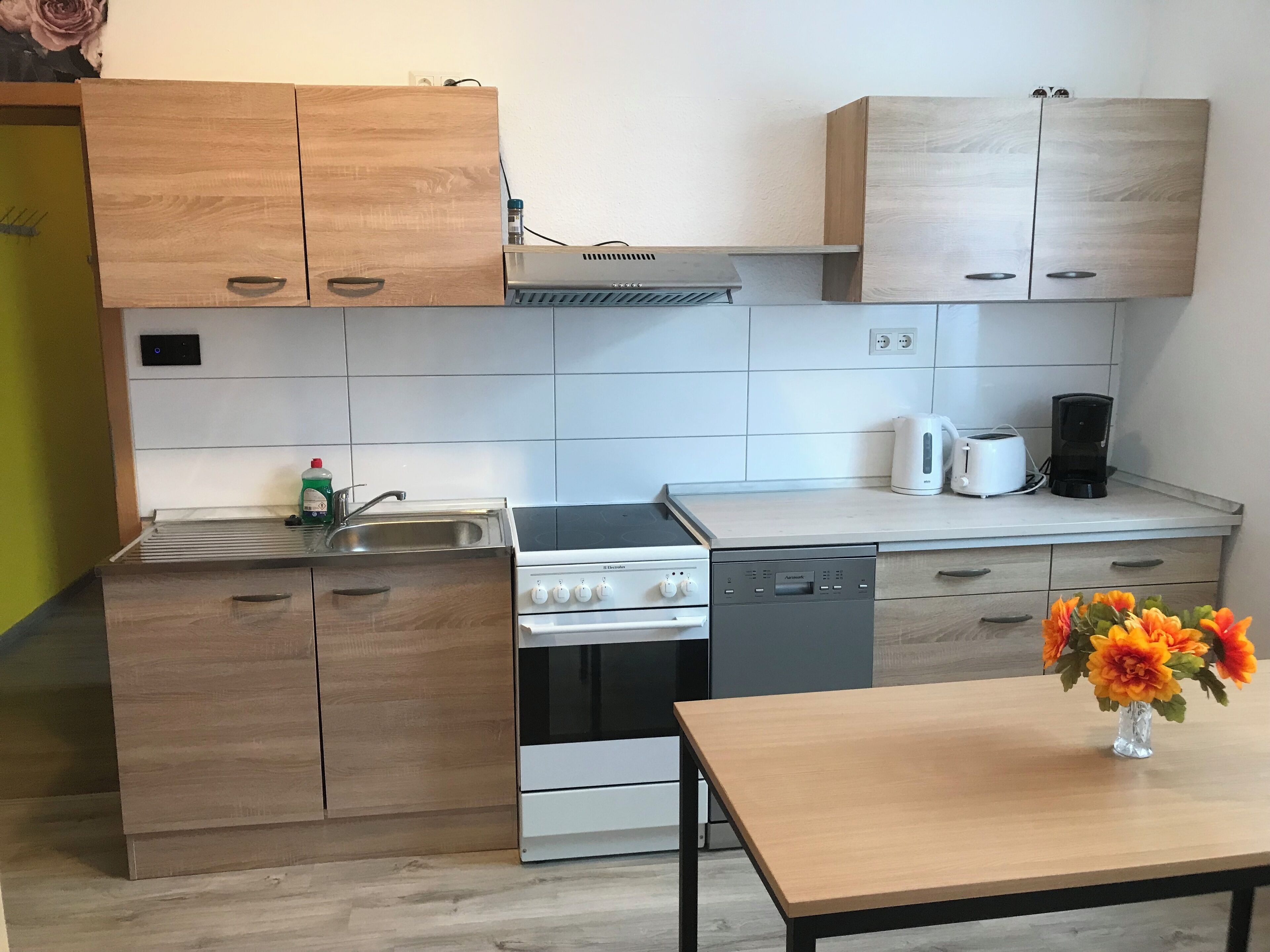 A modern kitchen with wooden cabinets, a built-in stove, a dishwasher, and a coffee maker on the counter.