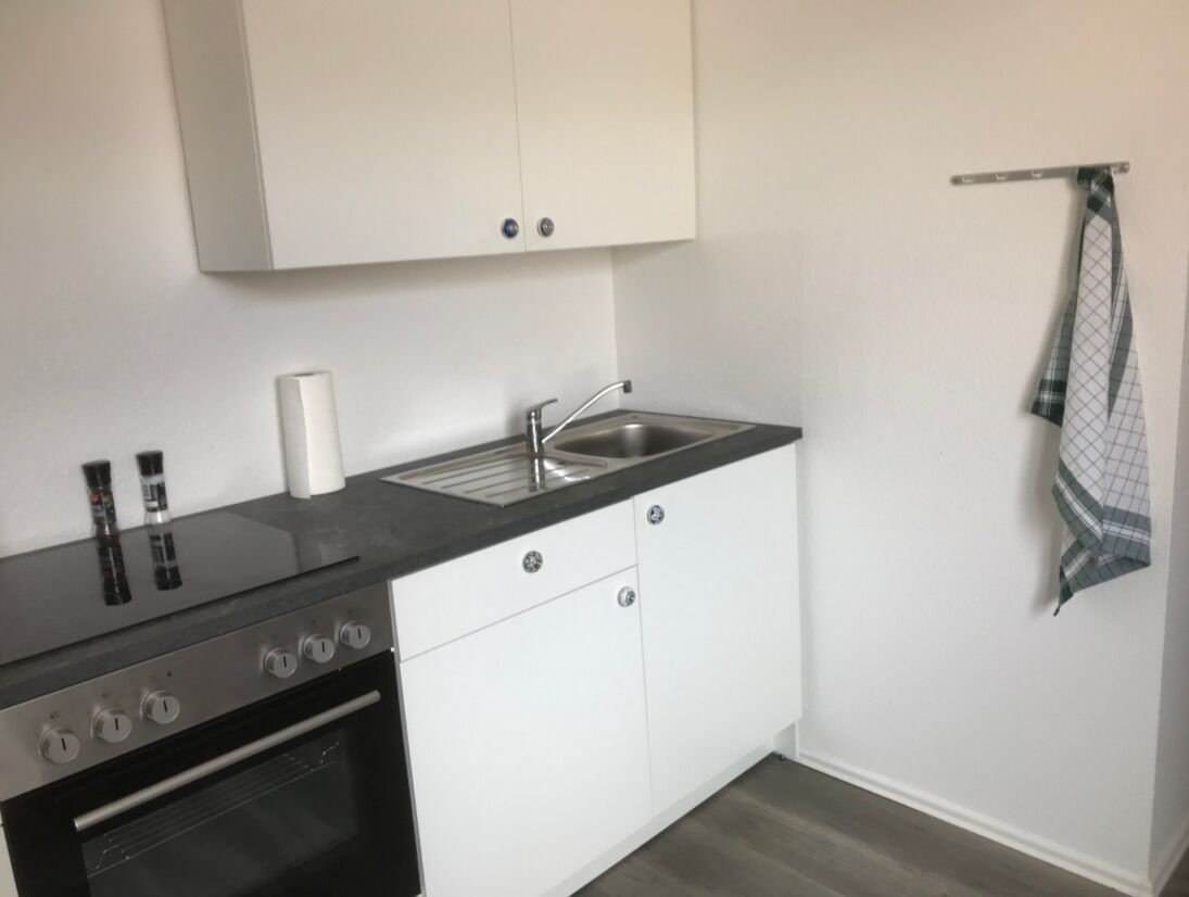 A compact kitchen with white cabinets, a black countertop, a stainless steel sink, and a small oven.