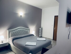 A modern bedroom with a tufted headboard, a bedside table with a lamp, a radiator, and a flat-screen TV mounted on the wall. - Rome Spacious 3 rooms&3 bath Métro Station 200 meters walk (Roma)