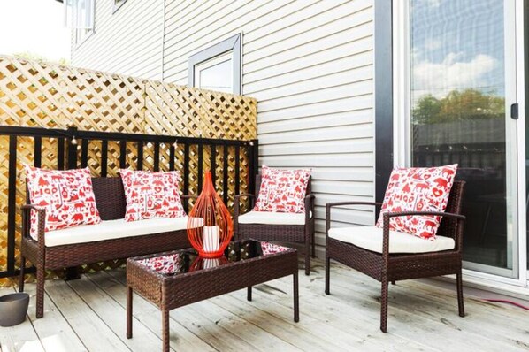 Une terrasse dotée de meubles en osier, d’un vase décoratif et d’une clôture à treillis.