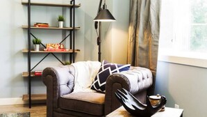 Un salon chaleureux avec un canapé en cuir, une bibliothèque, une lampe sur pied et un vase décoratif posé sur une table d’appoint.