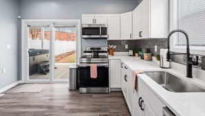 A modern kitchen with white cabinets, stainless steel appliances, and a large window. - Hot Tub - N64 - Mins to Downtown - Sleeps 8 (Cleveland)