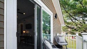 A covered patio with two wicker chairs, a sliding glass door leading to an interior space, and a white fence. - Hot Tub - N64 - Mins to Downtown - Sleeps 8 (Cleveland)