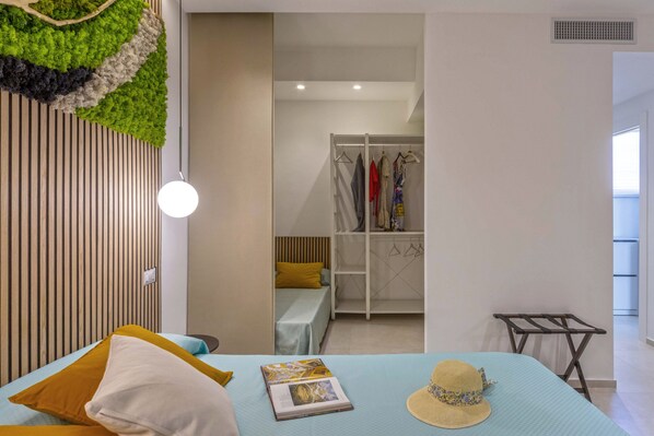 Un dormitorio con cama, lámpara colgante, armario y tendedero.