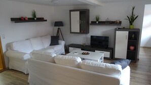 A modern living room with a white sofa, a coffee table, a TV, and decorative items on shelves.