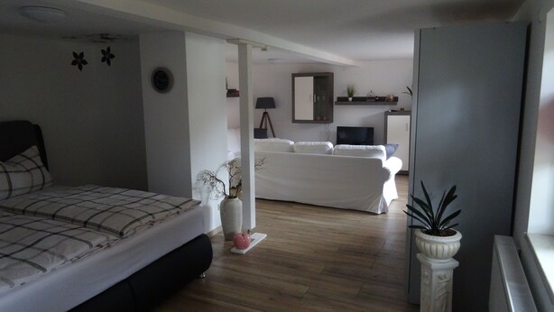A bedroom with a bed, a white sofa, a small table, and a potted plant.