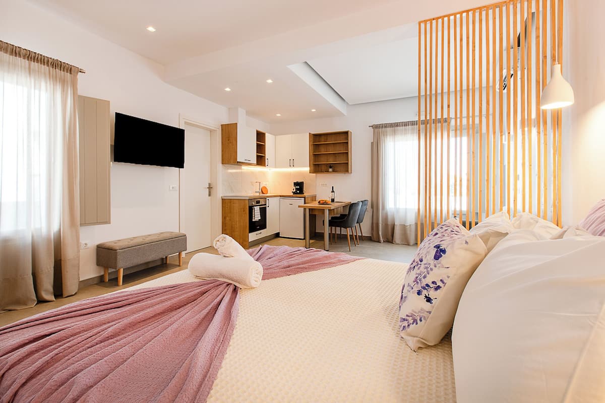 A modern hotel room with a large bed, a desk, and a kitchenette.