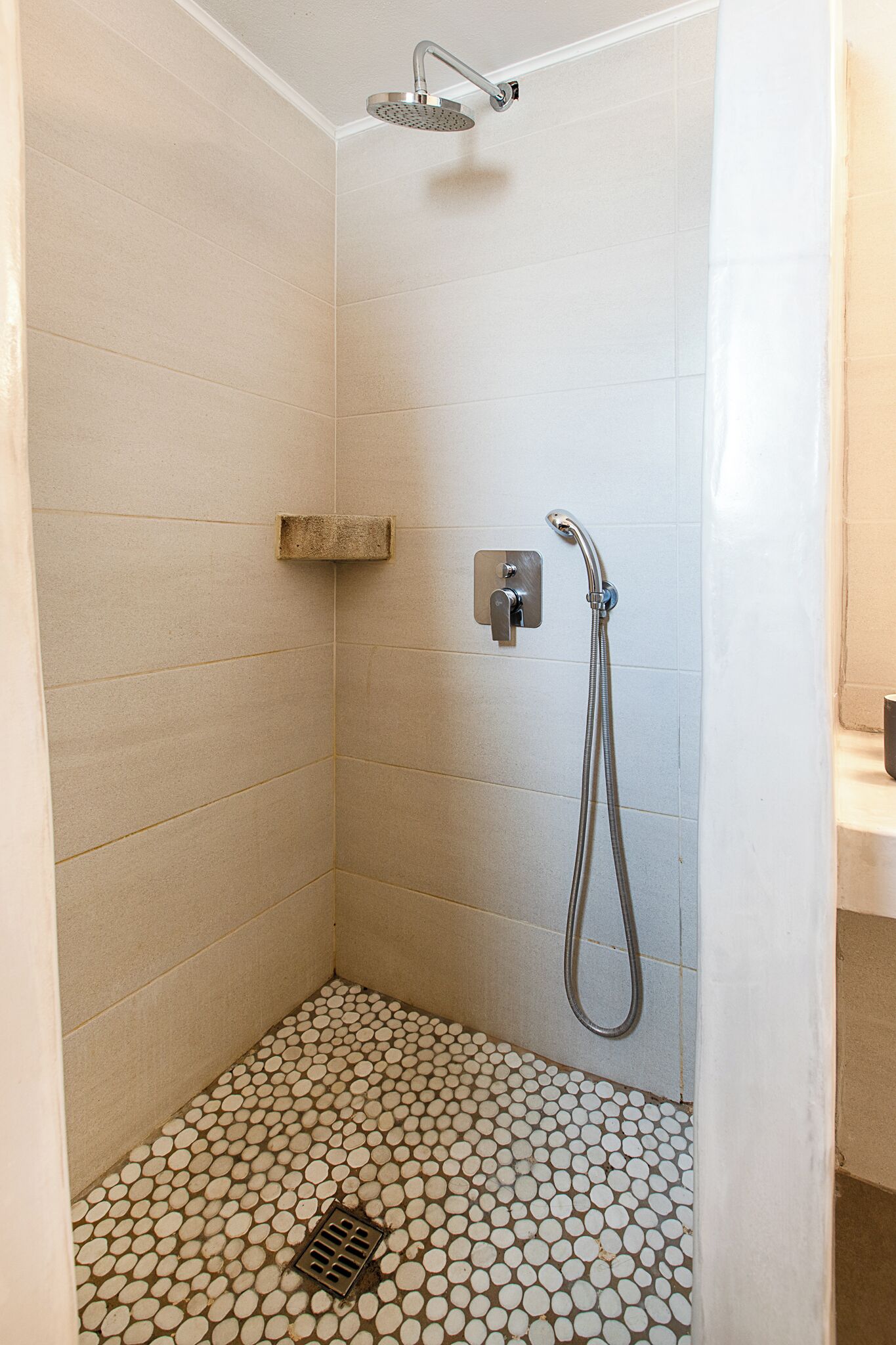Une petite douche carrelée, dotée d’un pommeau de douche à main et d’un robinet fixé au mur.