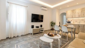 En moderne stue med et fladskærms TV, et spiseområde med stole, en sofa og et køkken med en mikrobølgeovn.