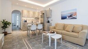 En moderne stue med en beige sofa, et spiseområde med hvide stole og et køkken med træskabe og et stålkøleskab.