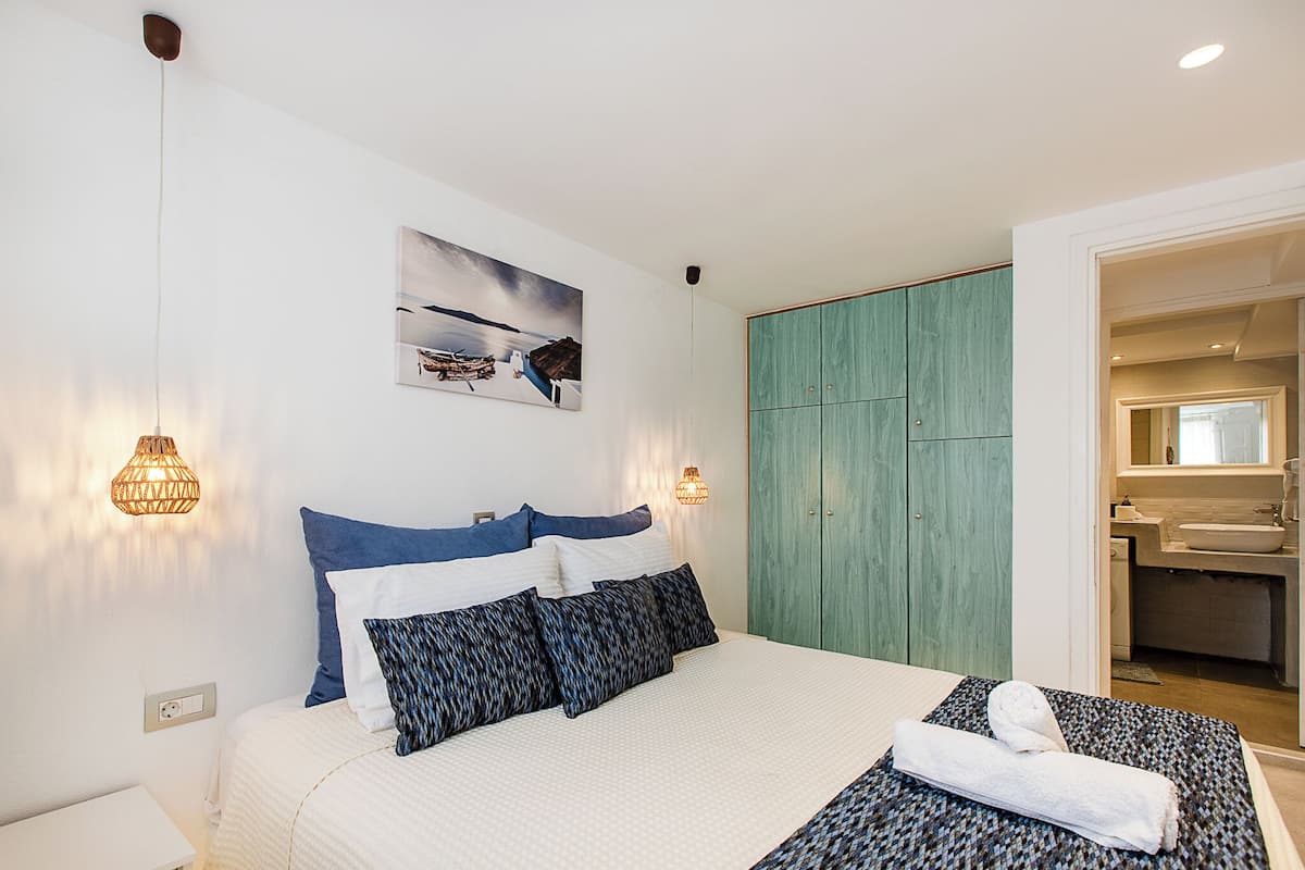 A neatly arranged bedroom with a bed, pillows, a wall-mounted picture, and a wardrobe.