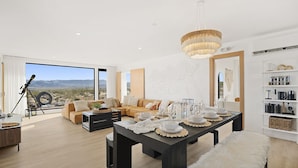 A spacious living room with a large dining table set for a meal, a comfortable sofa, and a telescope on a tripod by the window. - Joshua Tree Off-Grid Container Home (Joshua Tree)