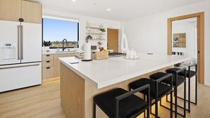 A modern kitchen with a large island, bar stools, and a view of the desert. - Joshua Tree Off-Grid Container Home (Joshua Tree)