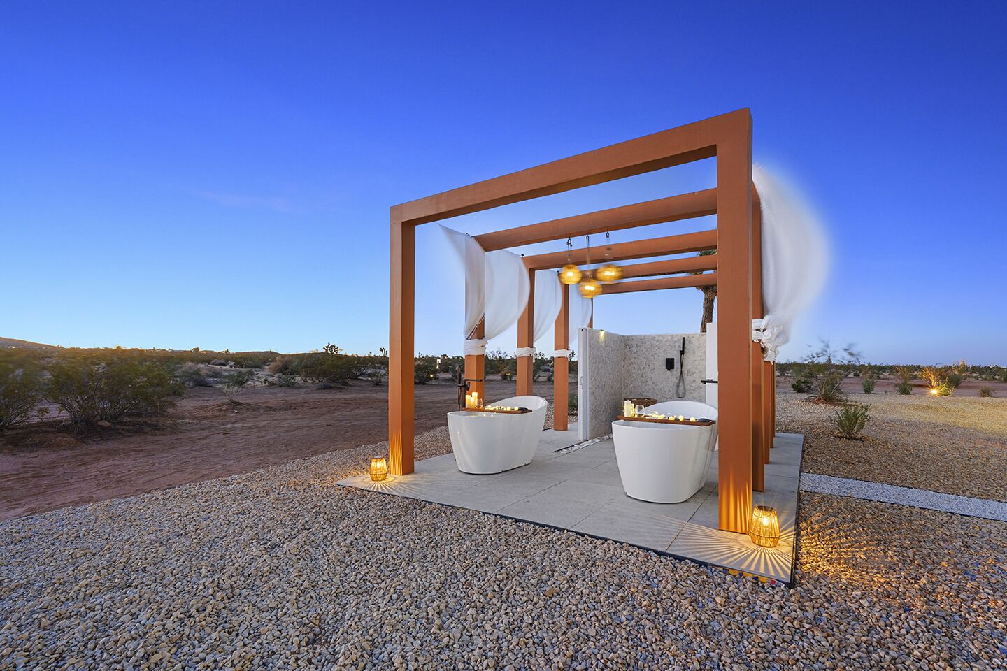 A spa area with a wooden pergola, two white tubs, and a stone wall.