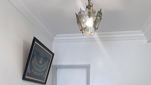 Ruokailutila, jossa on pitsillä koristeltu pöytäliina, kuvioiduilla tyynyillä varustetut puutuolit, koristeellinen maljakko ja kattokruunu.