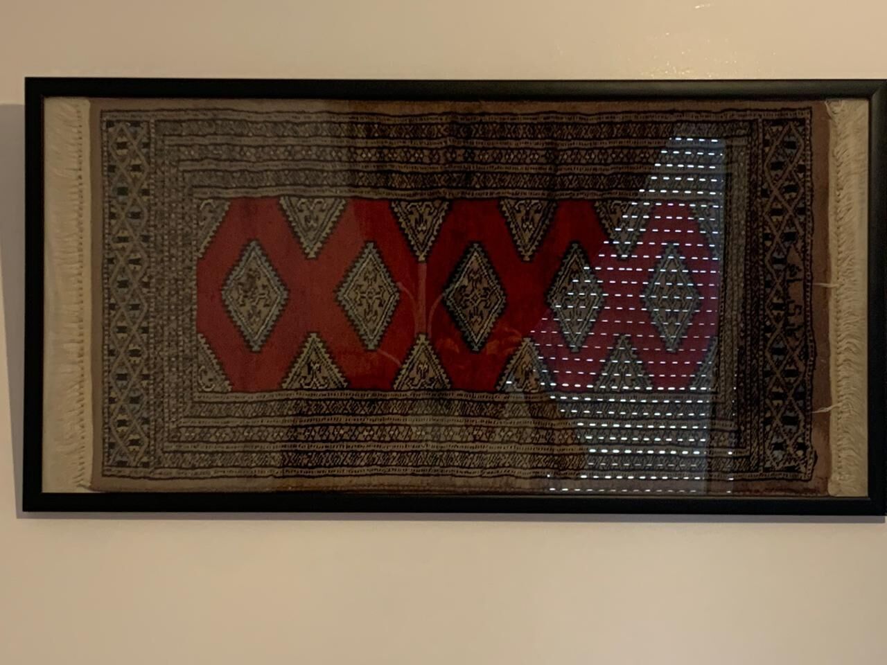 A framed textile artwork with geometric patterns and a central red motif.