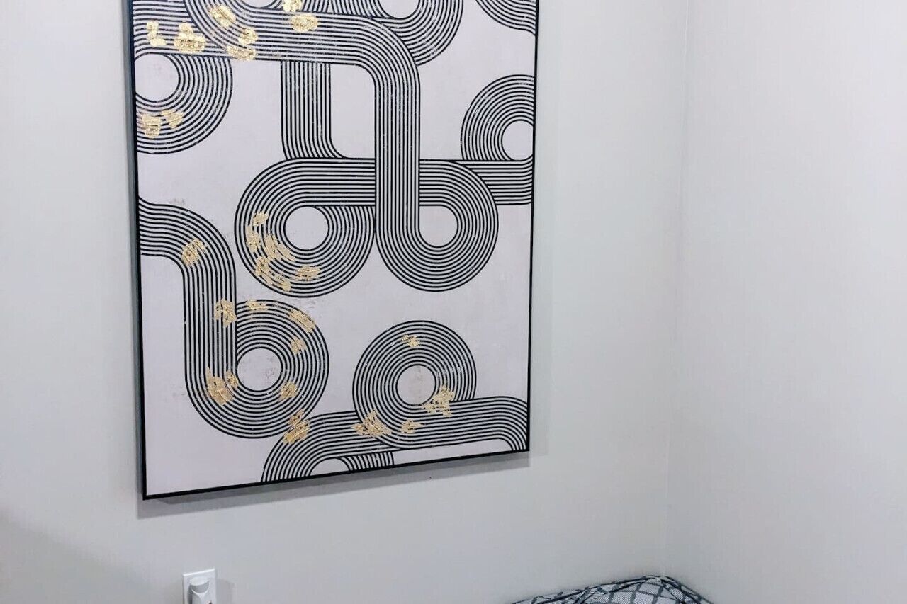 Obra de arte abstracta enmarcada, con patrones blanco y negro y detalles dorados sobre fondo blanco.